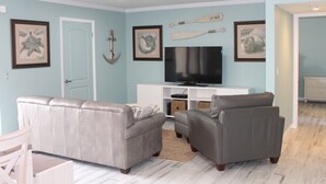 Ein Wohnzimmer mit grauem Sofa, einem Flachbildfernseher und gerahmten Kunstwerken an den Wänden.