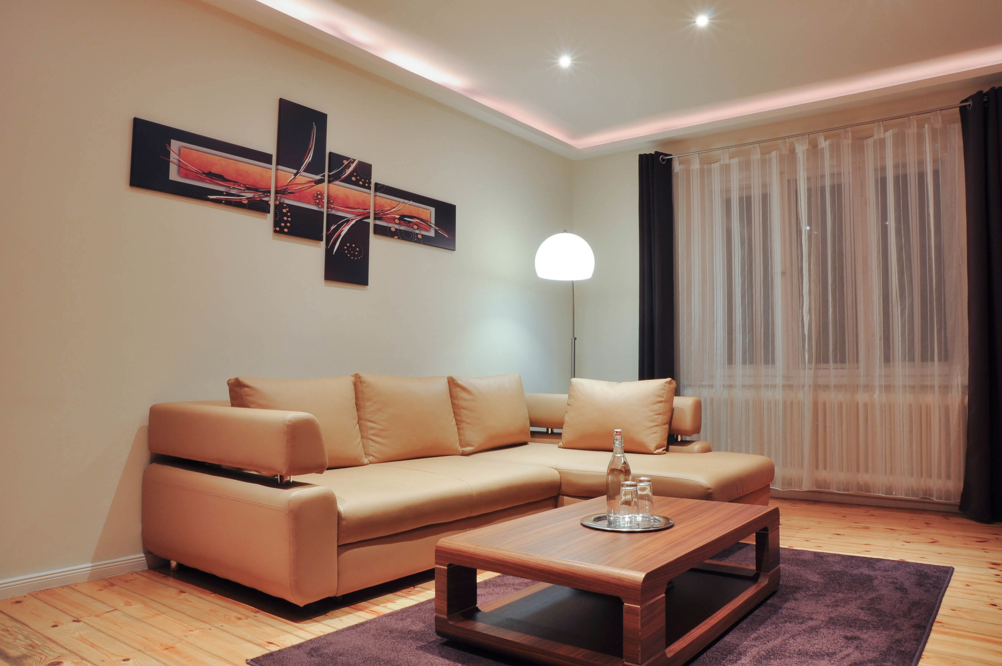 Ein modernes Wohnzimmer mit einem beigefarbenen Ecksofa, einem Holztisch und einer Stehlampe.