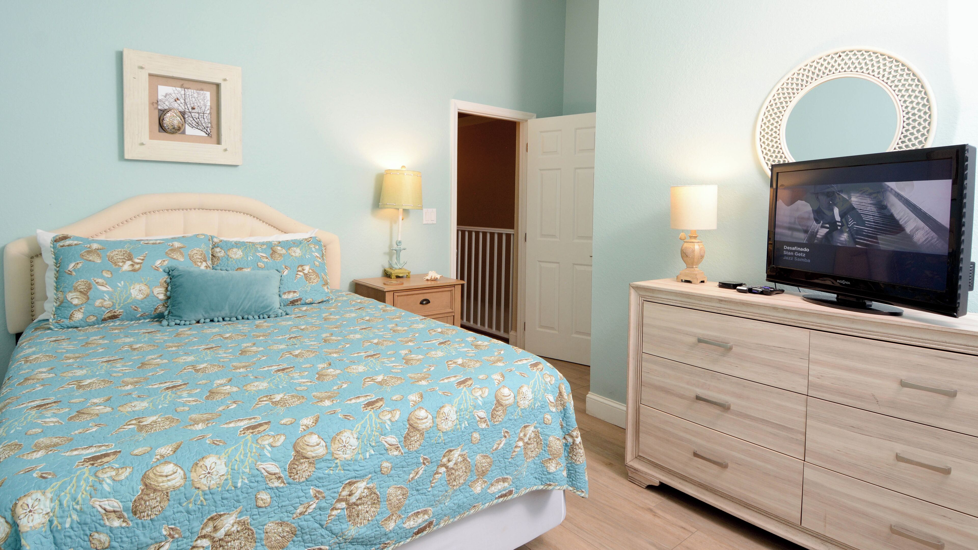 Une chambre à coucher comprenant un lit, une commode, un téléviseur et une porte donnant sur une salle de bain.