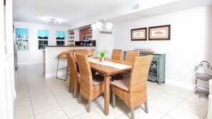 A dining area with a wooden table and wicker chairs, a kitchen in the background, and a decorative metal basket on the right. - 701 Mariners Club Live the Florida Keys dream! (Key Largo)