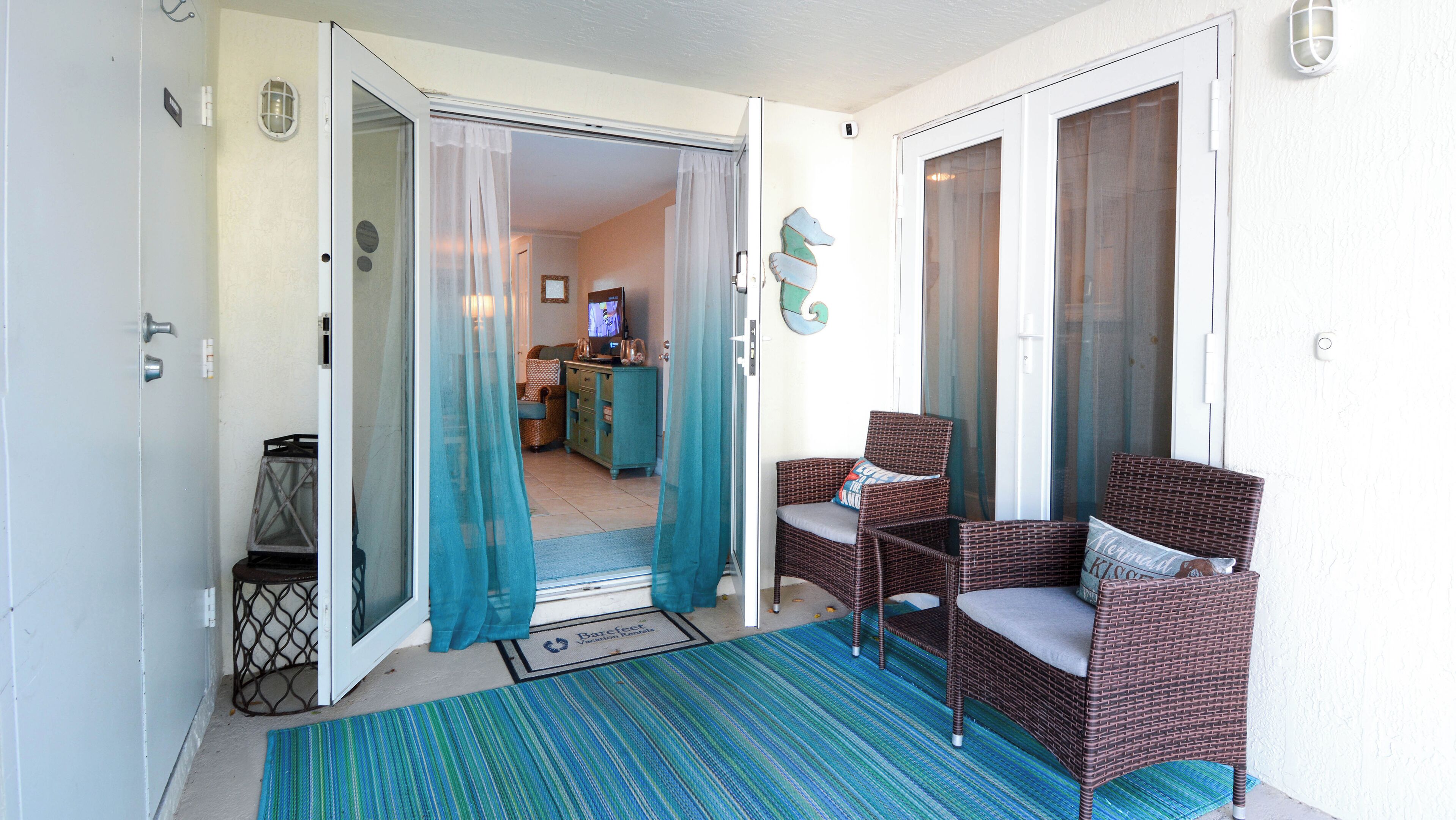 A room with a sliding glass door, wicker chairs, a television, and a kitchen area visible through the door.