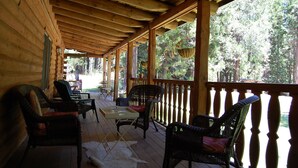 A covered porch with wicker furniture and a wooden railing, overlooking a forested area. - PAPA BEAR'S LODGE -Best Log Cabin in Nevada City Sleeps up to 10.  (Nevada City)