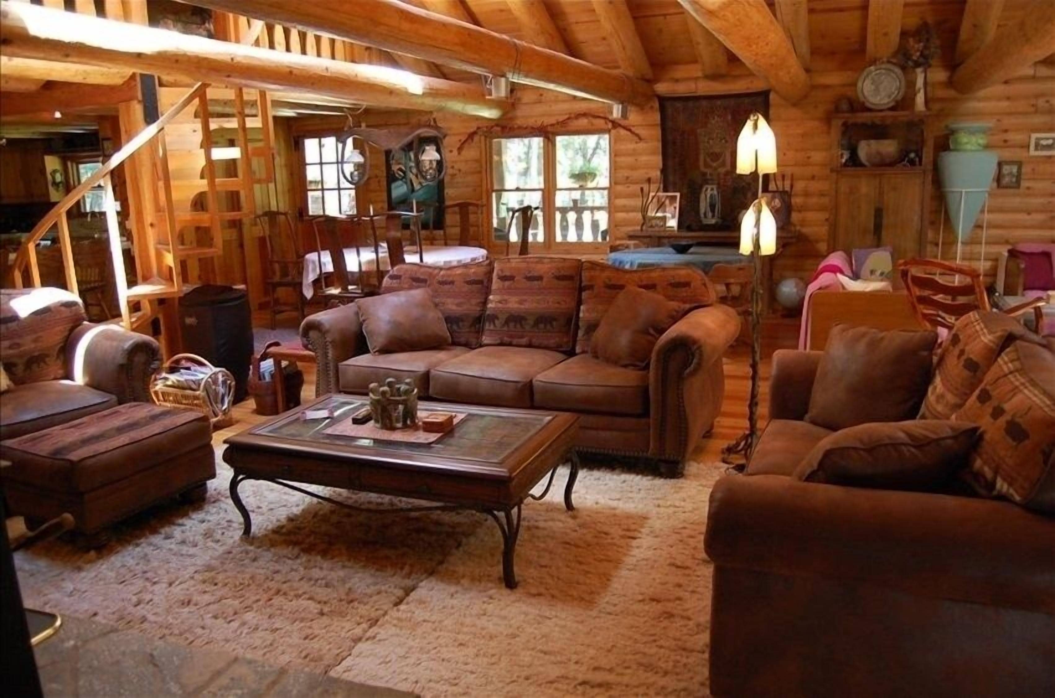 A cozy log cabin interior with a wooden staircase, a large brown leather sofa, a wooden coffee table, and a rustic decor style.