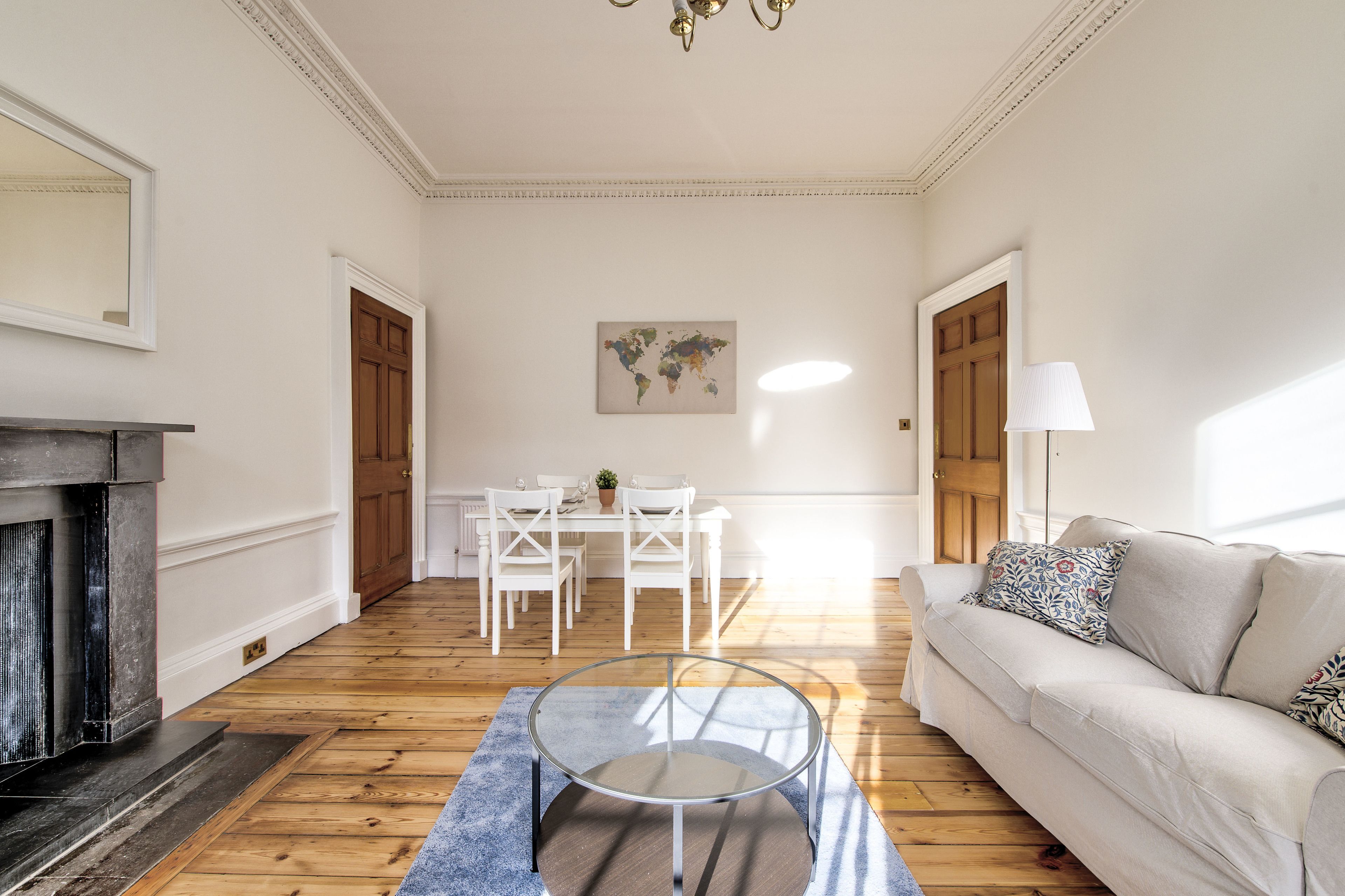 Een woonkamer met een ronde glazen salontafel, een bank, een open haard, een eettafel met stoelen en een wereldkaart aan de muur.