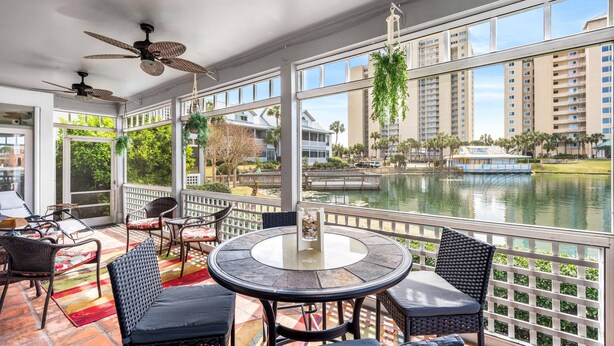A sunlit outdoor patio with a round table and chairs, overlooking a body of water and high-rise buildings.