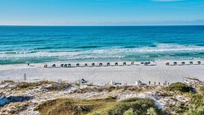 A beach with umbrellas lined up in rows, a sandy shore, and the ocean in the background.