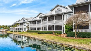 A row of modern, two-story houses with balconies, a canal in front, and well-maintained lawns.