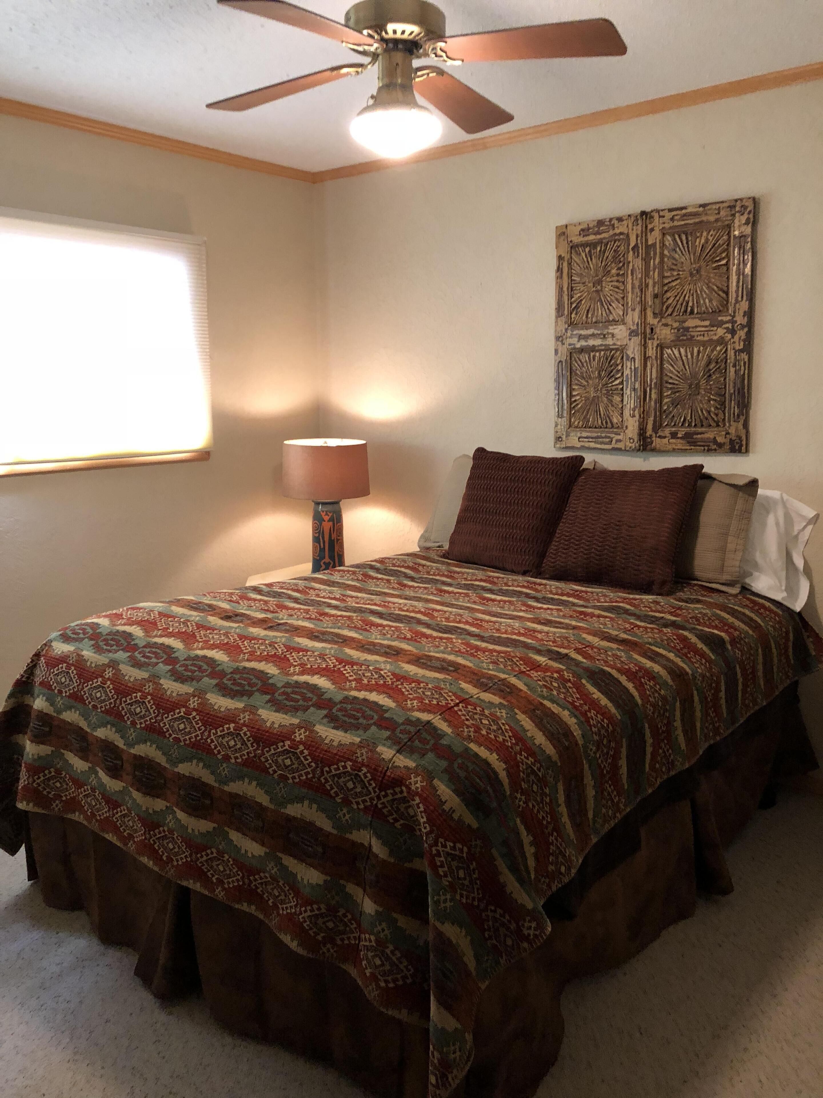 A bedroom with a bed, a ceiling fan, a wall-mounted lamp, and a decorative panel.