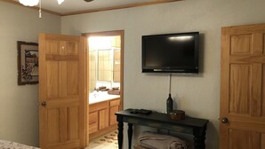 Una camera da letto con un letto, una porta in legno, un televisore su un mobile e un tavolino con un cesto.