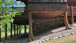 A wooden deck with a stone wall, supported by wooden pillars, and surrounded by a gravel path.