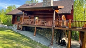 A log cabin with a stone chimney, wooden deck, and a stone foundation.