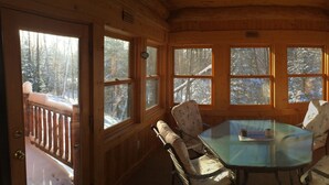 A wooden cabin with a glass table and chairs, large windows, and a deck area.