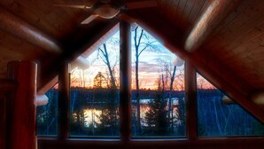 A room with a large window offering a view of trees and a sunset.