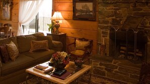 Un salon chaleureux avec un plafond en bois, une cheminée en pierre, un balcon et une grande fenêtre avec des rideaux.