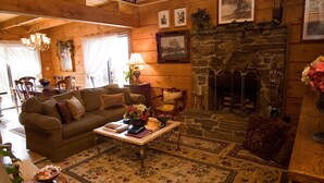 Un salon chaleureux avec une cheminée en pierre, des murs en bois et un tapis à motifs floraux.