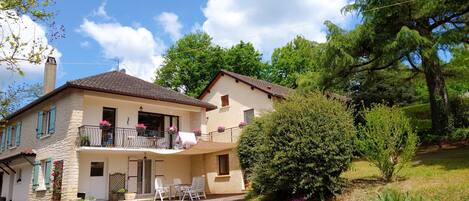 Une maison à deux étages avec un balcon, un petit patio avec des chaises et un jardin.