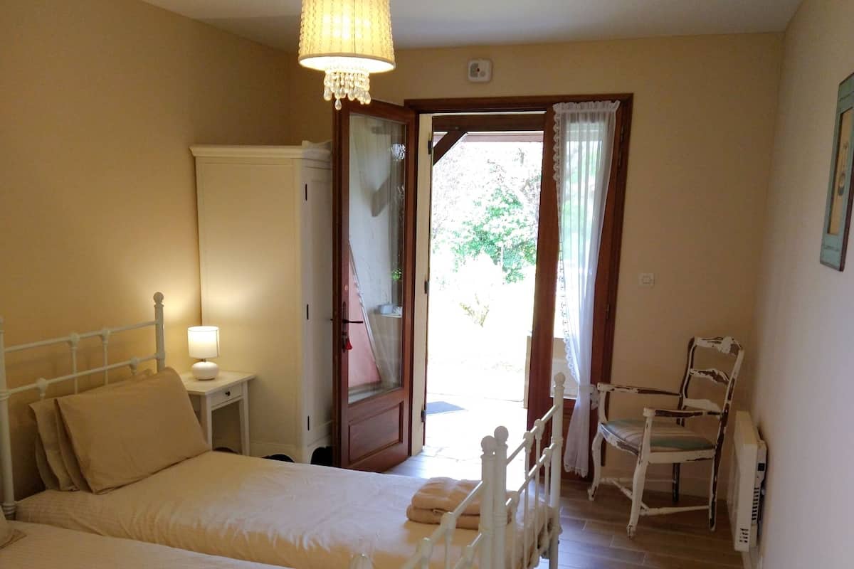 Un dormitorio con dos camas, una mesita de noche con lámpara, una silla y un radiador.