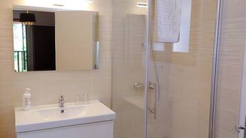 Un bagno moderno con doccia vetrata, un mobile lavabo bianco con specchio e pavimento in legno.