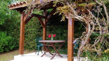 Une pergola en bois, avec une table et des chaises en dessous, entourée d’une végétation luxuriante.