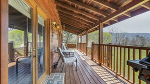 Una terrassa de fusta amb zona coberta, una cadira i una barbacoa.