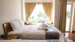 Camera d'albergo con due letti, una testiera in legno, un telefono sul comodino e vista su palme attraverso la finestra.
