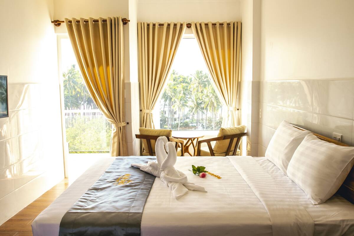 Habitación de hotel con cama, una mesa y sillas, televisor y vistas a palmeras.