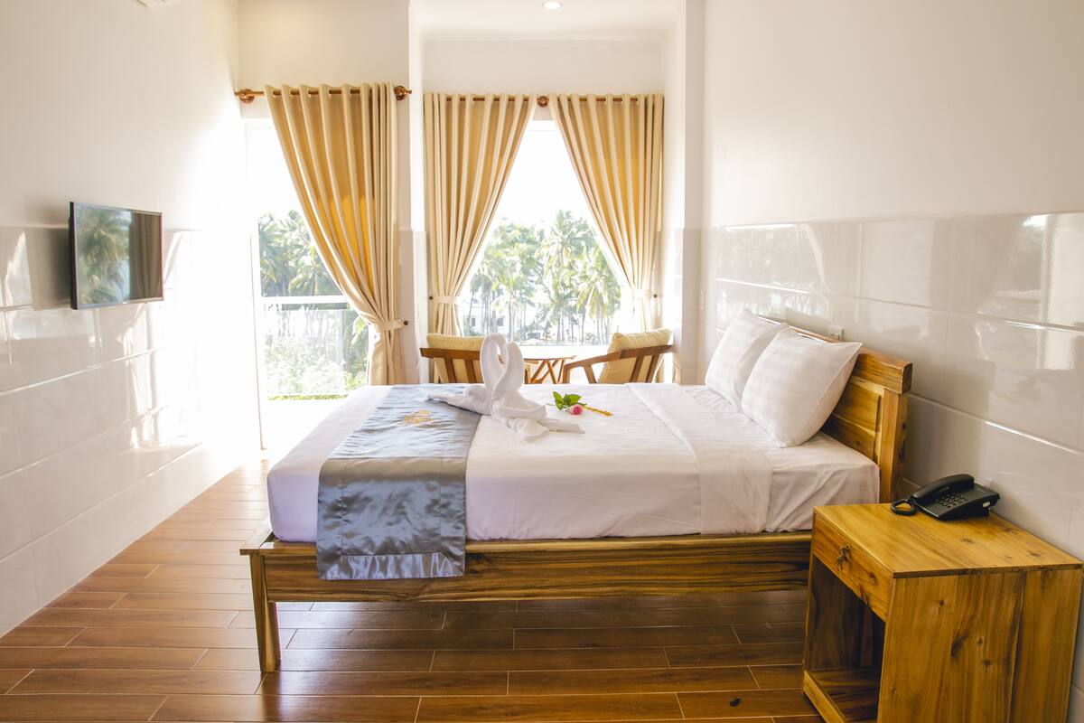 Habitación de hotel con una cama de madera, una mesita de noche con teléfono y un televisor montado en la pared.