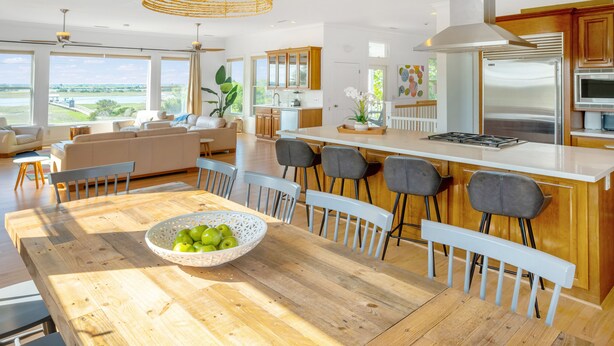 A modern kitchen with a wooden dining table, bar stools, and a large island. - Water's Edge - Amazing Sunset Views and Short Walk to the Beach. (Isle of Palms)