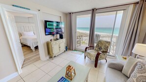 A hotel room with a bed, a television, a balcony with a view of the beach, and a chair.