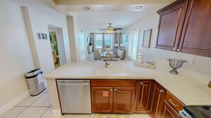 A modern kitchen with a dishwasher, wooden cabinets, a ceiling fan, and a view to the dining area.