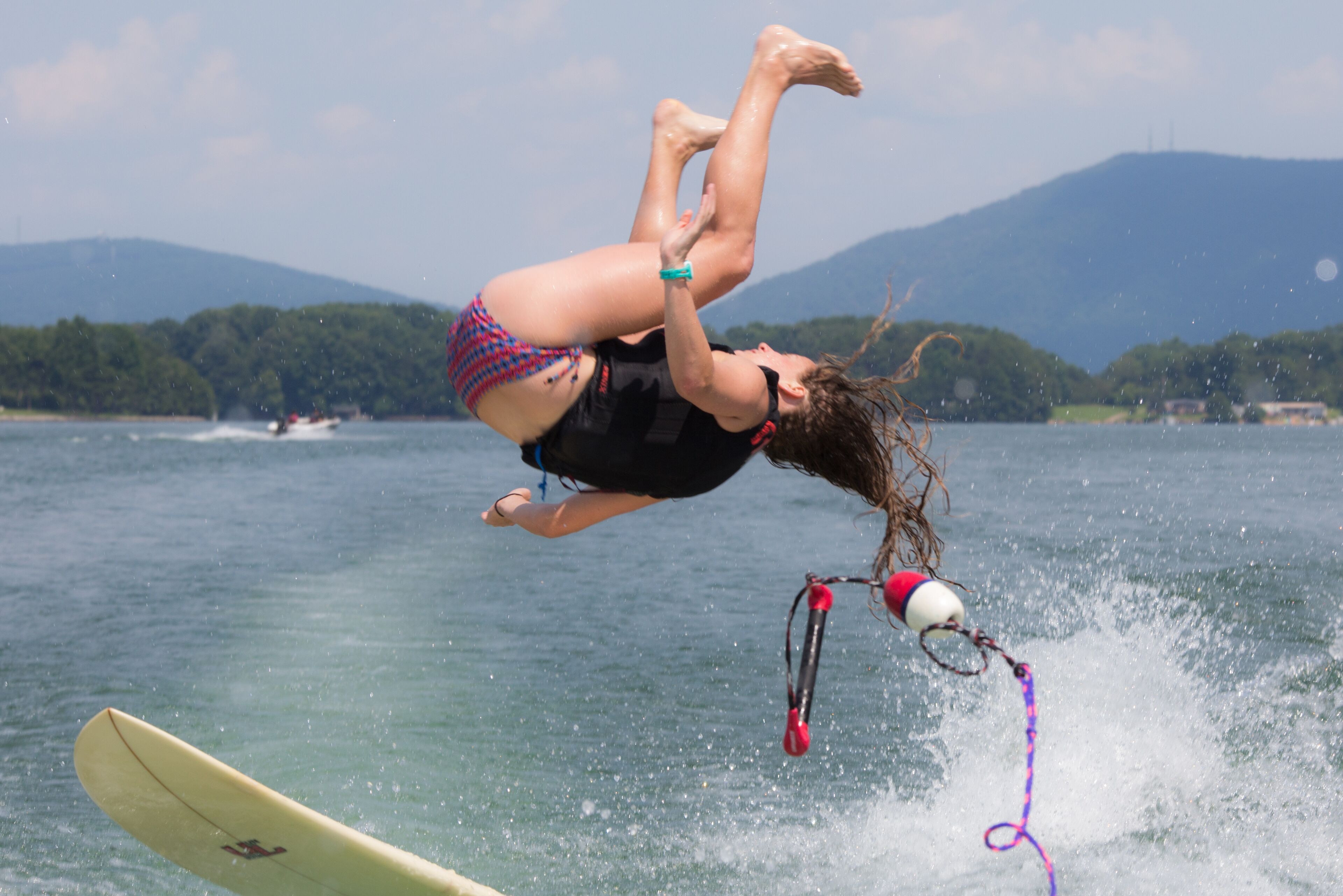 A person performing a backflip on a wakeboard in a body of water with mountains in the background.