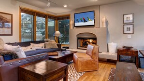 Una sala de estar acogedora con chimenea, ventanas amplias, televisor y sofá.