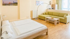 A modern hotel room with a bed, a green sofa, a coffee table, and a view of a cityscape through the window. - Apartments Atomis Hotel Düsseldorf City (Düsseldorf)