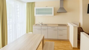 A modern kitchen with white cabinets, a wooden countertop, and a built-in oven. There is a window with sheer curtains and a light fixture above the counter. - Apartments Atomis Hotel Düsseldorf City (Düsseldorf)