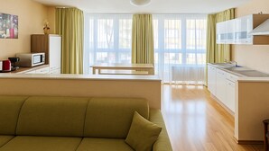A modern living room with a green sofa, a kitchen with a white countertop, and large windows with green curtains. - Apartments Atomis Hotel Düsseldorf City (Düsseldorf)