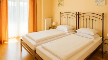 Ein Doppelbett mit Metallgestell in einem Zimmer mit Holzboden und einem fensterbelaubten Fenster.