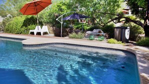 A swimming pool with clear water, surrounded by greenery and outdoor furniture. - Studio Guesthouse In Resort Setting (Phoenix)