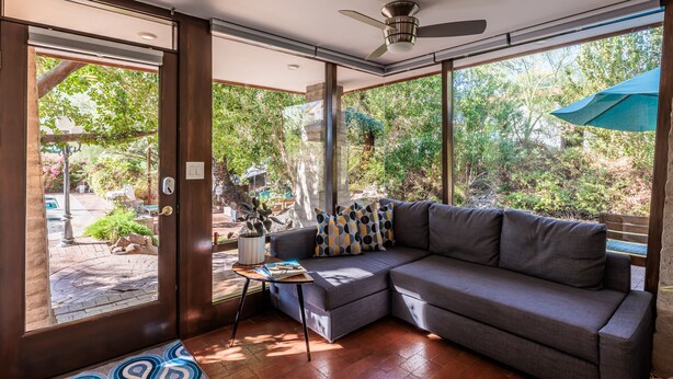 A modern living room with a sectional sofa, a ceiling fan, and large windows offering a view of the outdoors. - Studio Guesthouse In Resort Setting (Phoenix)