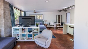 A modern bedroom with a large bed, a TV, a white console table with books, a patterned armchair, and a desk with a chair. - Studio Guesthouse In Resort Setting (Phoenix)