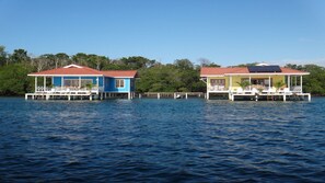 Zwei Ferienhäuser am Wasserufer mit roten Dächern, weißen Geländern und Holzterrassen.
