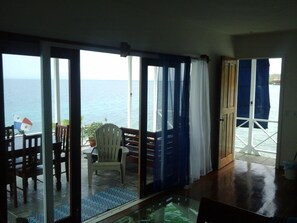 Ein Zimmer mit Meerblick, ein Essbereich mit Stühlen und Tisch sowie eine Glastür, die nach draußen führt.