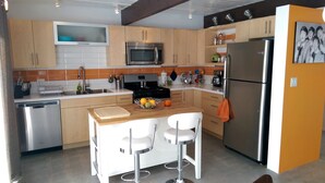 A compact kitchen with a microwave, stove, sink, and a refrigerator. There is a small dining area with two chairs and a table. - A Mid-Century Modern Alexander Home Oasis (Lively Music-Themed Decor). (Palm Springs)