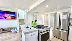 A modern kitchen with a built-in oven, a stainless steel refrigerator, and a flat-screen TV mounted on the wall.