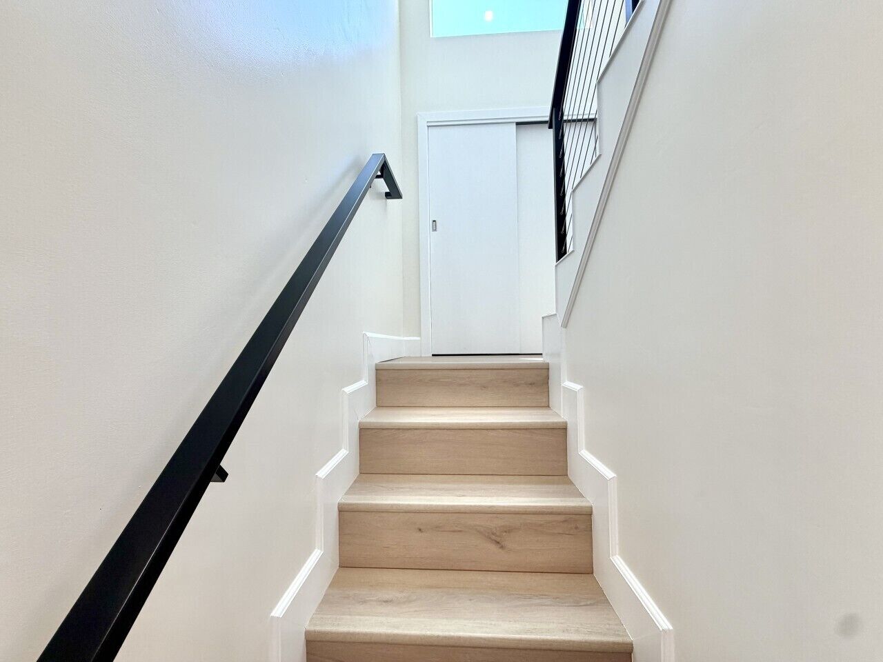 Eine Treppe mit hölzernen Stufen und einem schwarzen Geländer, die zu einer weißen Tür führt.