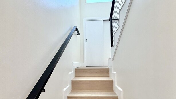A staircase with wooden steps and a black handrail, leading to a white door at the top.