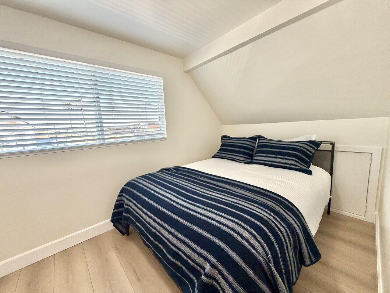 A bedroom with a bed, a window with blinds, and a radiator.
