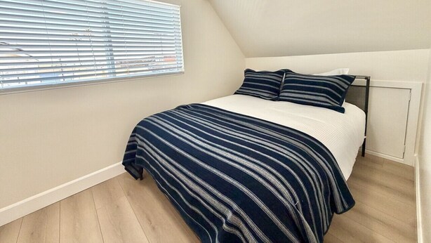 A bedroom with a bed, a window with blinds, and a radiator. - NEW July 2026 Remodel! Triton`s Castle Overlooking Beach and Bay! (San Diego)