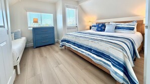 A bedroom with a bed, a dresser, a bench, and two windows.