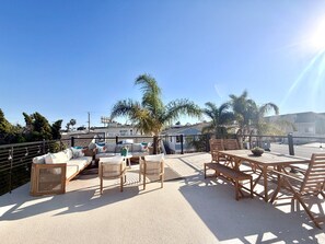 An outdoor patio with a sofa, chairs, and a table, surrounded by a fence and palm trees.