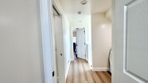 A hallway with wooden flooring, white walls, and a door leading to a room.
